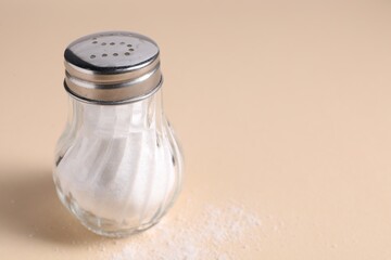 Natural salt in shaker on beige background, closeup. Space for text