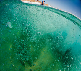 The perspective of a surfer surrounded by the intense turquoise hues and effervescent textures of a wave's barrel, under a clear sky