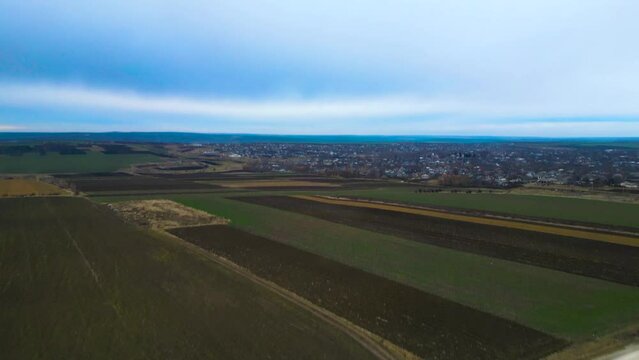 Aerial drone shot - A Car driving through a dirt road through hills in Moldova with a town in the background