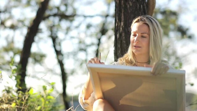 Woman with long hair painting under tree in outdoor leisure event