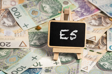Black writing board on a wooden frame with the inscription "E5", Polish zloty PLN banknotes scattered in the background (selective focus)