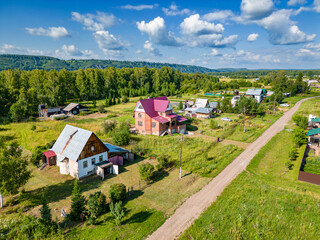 village street with sparse buildings and a lot of green vegetation - trees and bushes surrounded by grass