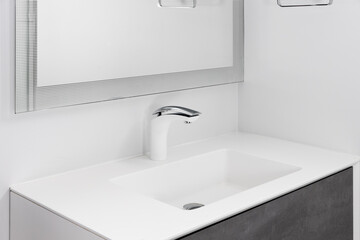 A bathroom faucet detail with a white and chrome faucet, white sink, and a dark grey cabinet.