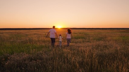 Mom dad kid daughter run together on nature. Family walks on green grass in meadow. Happy family, child, are walking in summer field, holding hands. Parents, child are walking in park at sunset.