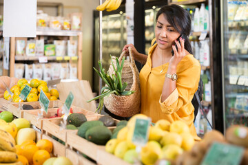 Positive woman choosing fruit and talking on mobile phone in a grocery store