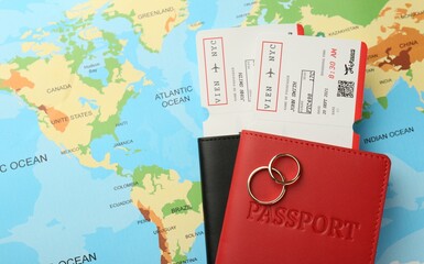 Honeymoon concept. Plane tickets, passports and golden rings on world map, top view