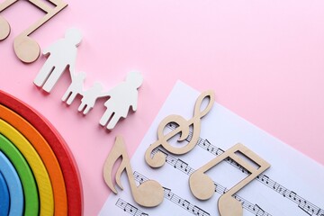 Baby songs. Music sheet, figures of family, wooden notes and toy rainbow on pink background, flat...