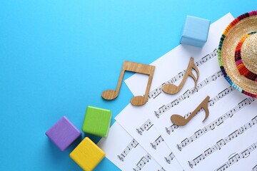 Baby songs. Music sheets, wooden notes, cubes and hat on light blue background, flat lay with space...