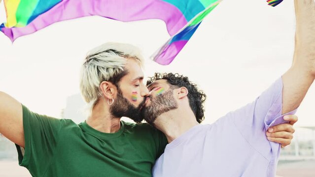 Gay couple kissing in love as they celebrate LGBT Pride Day parade with a rainbow flag. Lesbian, gay, bisexual, transgender social movements. Concept of happiness freedom love same-sex couple.