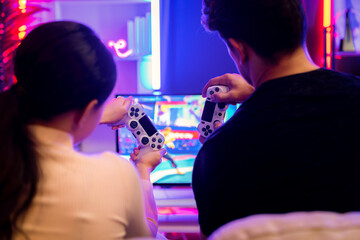 Couple joyful player video game on TV using joysticks at back side, playing fighting game with winner together raising fist up in studio room in red neon light at comfy living home place. Postulate.