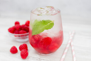 Cold refreshing lemonade drink or cocktail made of water, raspberry and mint. Served drinking glass with ice cubes. On white wooden backgrond with copy space. 