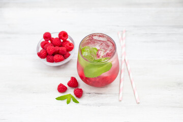 Cold refreshing lemonade drink or cocktail made of water, raspberry and mint. Served drinking glass with ice cubes. On white wooden backgrond with copy space. 