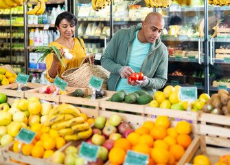 Hispanic married couple shopping together in grocery store, choosing fresh vegetables and fruits
