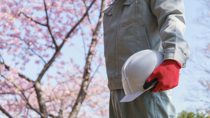 桜の花とヘルメットを持つ作業服の男性