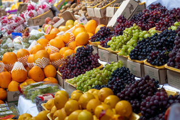 A colorful array of fresh fruits including grapes, oranges, and kiwis fills the frame at a bustling...