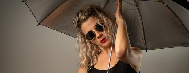 woman WITH WHITE CURLERS with an open umbrella over her head wearing a BLACK suit posing in PHOTO STUDIO