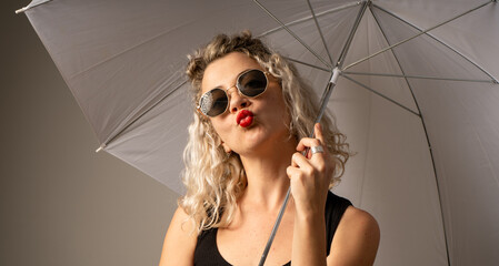 woman WITH WHITE CURLERS with an open umbrella over her head wearing a BLACK suit posing in PHOTO STUDIO