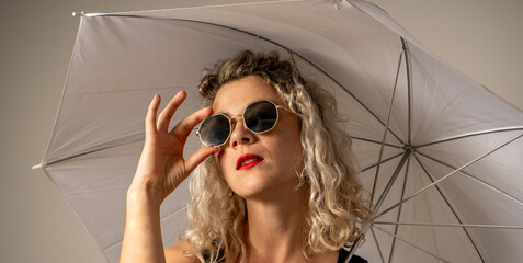 woman WITH WHITE CURLERS with an open umbrella over her head wearing a BLACK suit posing in PHOTO STUDIO