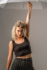 woman WITH WHITE CURLERS with an open umbrella over her head wearing a BLACK suit posing in PHOTO STUDIO