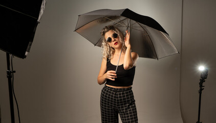 woman WITH WHITE CURLERS with an open umbrella over her head wearing a BLACK suit posing in PHOTO STUDIO
