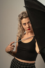 woman WITH WHITE CURLERS with an open umbrella over her head wearing a BLACK suit posing in PHOTO STUDIO