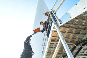 uprisen angle engineer working in fieldwork at outdoor with wind turbine and clear sky. Workers check construction. Wind turbines for electrical clean energy and environment sustainability.