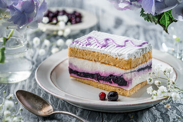 Piece of crem mousse cake with berries on light grey background with berries and violet flowers. Sweets, dessert and pastry, top view