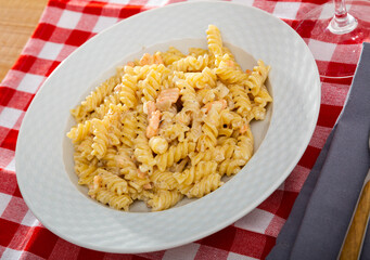 Close up of tasty warm pasta with smoked salmon at plate on table with checkered tablecloth