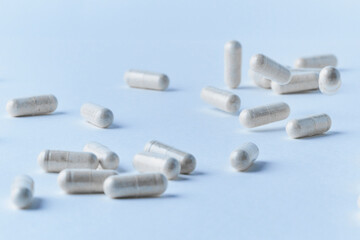 Pharmaceutical clear capsules filled with white probiotics powder closeup on light blue background dropped and spilled with petri dish 