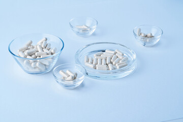Pharmaceutical clear capsules filled with white probiotics powder closeup on light blue background dropped and spilled with petri dish 