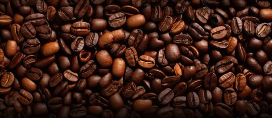 Fototapeta premium A stack of coffee beans is prominently displayed, showcasing the rich brown hues and varying sizes of the beans. The beans are clustered together, creating a textured and aromatic scene.