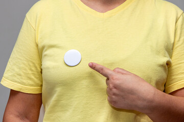 Woman in yellow shirt pointing at a shiny round button. Isolated pin badge mockup
