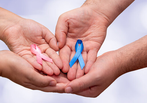 Two hands holding two Pink and Blue ribbons for the Pink October and Blue November campaigns to support life and raise awareness about cancer. Man's hand and woman's hand