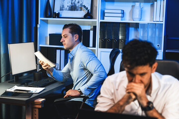 Colleagues concentrating on their job task at night home office behind desk while another man with...