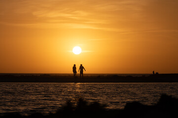 Man and woman staying and looking at sunset on ocean beach, orange sky, silhouettes of people on vacation