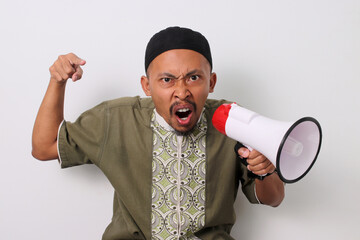 Angry Indonesian Muslim man in koko and peci shouts into a megaphone, pointing his finger at the...