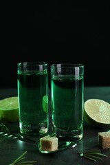 Absinthe in shot glasses, spoon, lime and brown sugar cubes on gray textured table, space for text....