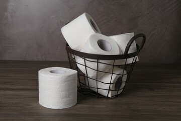 Soft toilet paper rolls in metal basket on wooden table