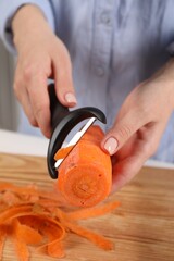 Woman peeling fresh carrot at table indoors, closeup