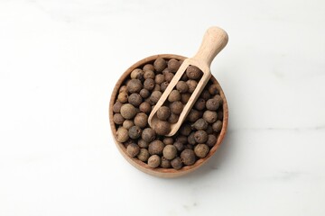 Dry allspice berries (Jamaica pepper) in bowl and scoop on white marble table, top view