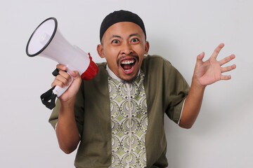 Excited Indonesian Muslim man in koko and peci holds a megaphone, announcing Ramadan sale...