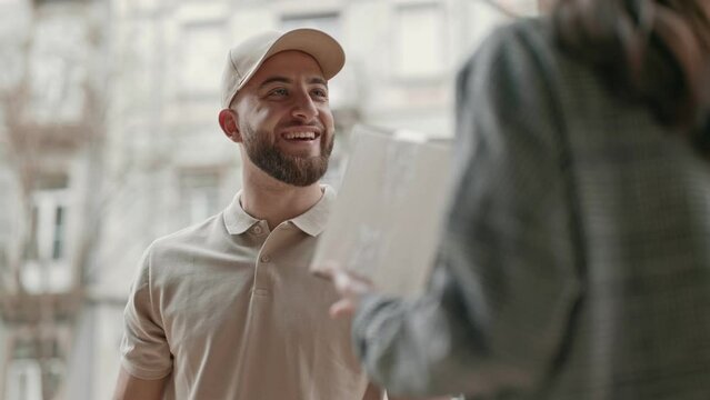 Friendly courier in cap giving a parcel to a customer on a city background, displaying efficient service.