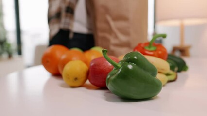 Unpacking healthy groceries. Fresh fruits and vegetables displayed prominently as they are taken out from a paper bag on a kitchen counter.