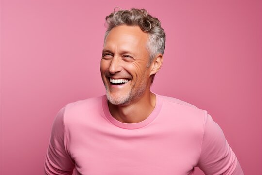 Handsome middle aged man laughing and looking at camera against pink background
