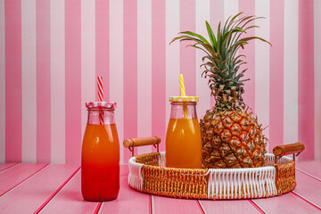 Pineapple, pineapple juice in cocktail bottles stands on a tray in the kitchen. Pink striped...