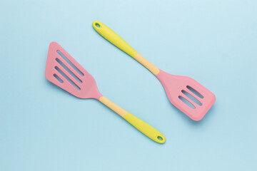 Two multicolored silicone kitchen spatulas on a blue background.