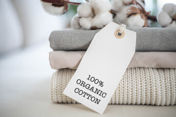 A neat stack of knitted clothing labeled 100% organic cotton. White background.