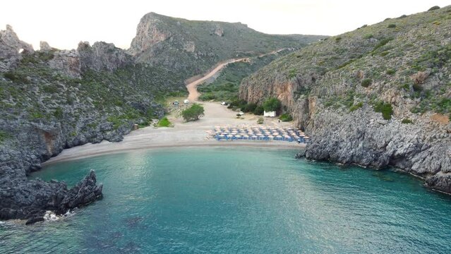 Chalkos Beach in Kythera, Greece, boasts sunbeds and sun umbrellas on its sandy shore. Crystal clear waters in a rocky gulf add to the beauty.