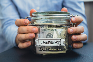 Female hands Saving Money In Glass Jar filled with Dollars banknotes. EMERGENCY transcription in...