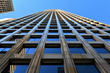 Looking up at a towering skyscraper against a clear blue sky